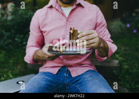 Close up of man working outdoors in the garden, eating lunch, sandwich. Businessman working remotely from homeoffice, thinking about new business or Stock Photo