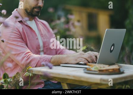 Man working outdoors in the garden, eating lunch, sandwich. Businessman working remotely from homeoffice, thinking about new business or creative idea Stock Photo
