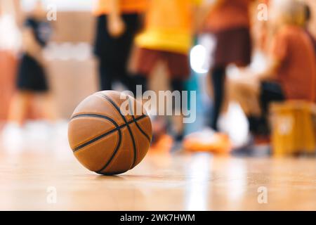 Basketball Ball On Hardwood Floor Youth Basketball Team in Background. Indoor Sports Training Unit for School Kids Stock Photo