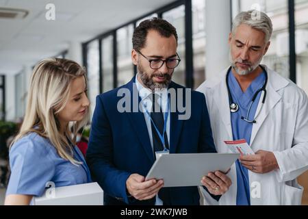 Pharmaceutical sales representative presenting new medication to doctors in medical building, showing on tablet. Hospital director of private medical Stock Photo