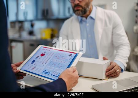 Pharmaceutical sales representative presenting new medication to doctor in medical building, holding tablet with presentation, graphs and statistics, Stock Photo