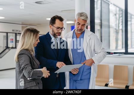Pharmaceutical sales representative presenting new medication to doctors in medical building, presenting on tablet. Hospital managers of private medic Stock Photo