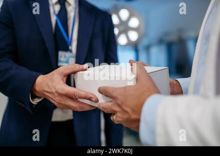 Pharmaceutical sales representative presenting new medication to doctor in medical building, holding and handing box with medication, drugs samples to Stock Photo