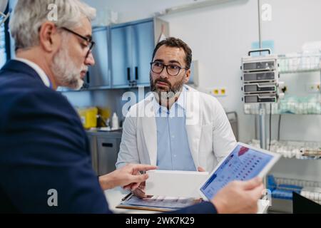Pharmaceutical sales representative presenting new medication to doctor in medical building, holding tablet with presentation, graphs and statistics, Stock Photo