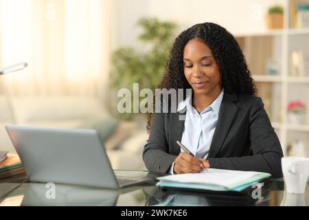 Tele worker working online with a laptop at home taking notes Stock Photo