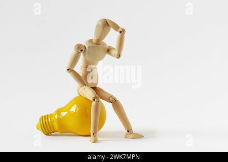 Wooden mannequin in thinking pose sitting on yellow light bulb - Concept of ideas and creative thinking Stock Photo