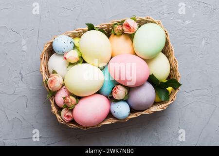 Happy Easter. Easter eggs in basket on colored table with yellow roses. Natural dyed colorful eggs background top view with copy space. Stock Photo