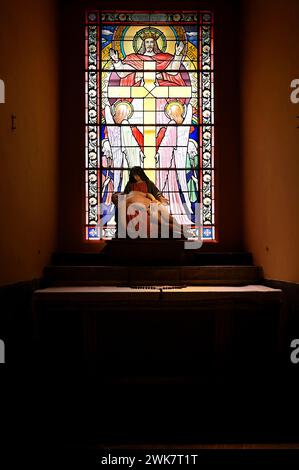 Statue of pieta, depicting the Virgin Mary contemplating the body of her Son, with stained glass of the risen Christ and cross held by two angels Stock Photo