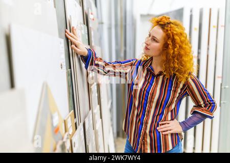 Portrait of buyer in bathroom store. Redhead woman is choosing tiles for her apartment. Stock Photo