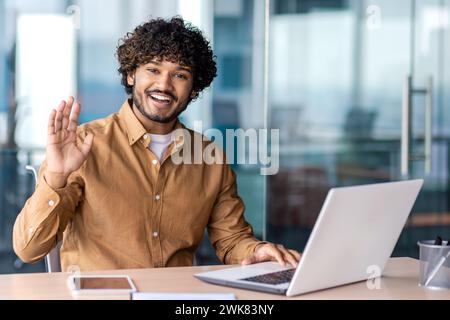 Portrait of a happy Indian young man working in the office. looks pleased at the camera, greets and waves. Stock Photo