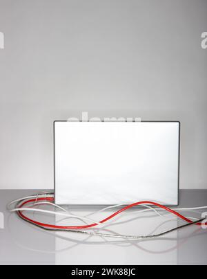 A laptop with cables on a desk on a grey background Stock Photo