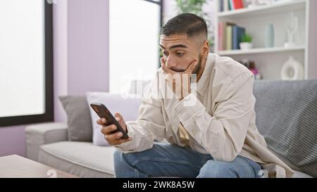 A pensive man using a smartphone in his modern living room, showing contemporary lifestyle and technology. Stock Photo