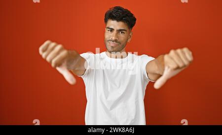 Handsome hispanic man giving thumbs down against a red wall isolated. Stock Photo