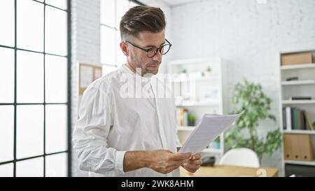 Attractive young hispanic male business manager, concentrated in reading an important document in the office, serious expression portraying success Stock Photo