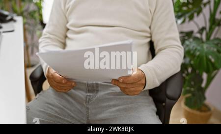 A latin man in an office examines documents, suggesting a professional, corporate setting for mature adult males. Stock Photo