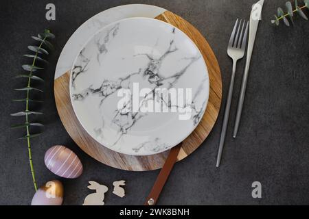 Easter table setting concept. Plate, easter eggs, cutlery and branches of eucalyptus on dark background table Stock Photo