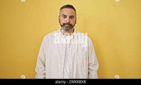 A mature hispanic man with grey beard stands confidently against an isolated yellow background. Stock Photo