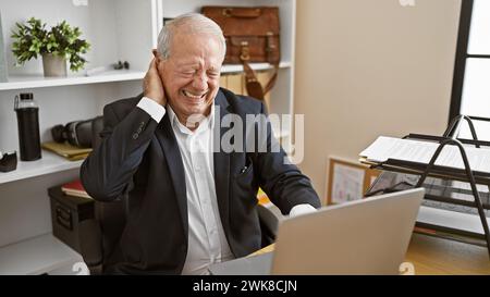 Stressed senior man suffering from cervical pain while working intensely on laptop in office Stock Photo