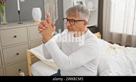 A middle-aged man gestures with his hands mimicking a gun in a contemporary bedroom setting. Stock Photo