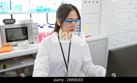 A young asian woman wearing safety glasses works focusedly in a modern laboratory setting. Stock Photo