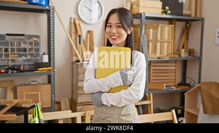 Smiling asian woman holding clipboard in carpentry workshop Stock Photo
