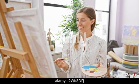 Smiling caucasian woman painting on canvas in a bright art studio Stock Photo