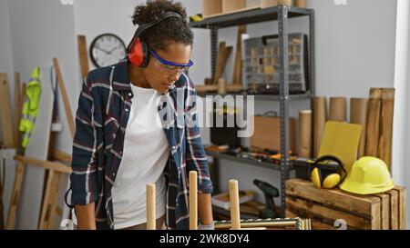 Young woman working attentively in a carpentry workshop with safety gear. Stock Photo