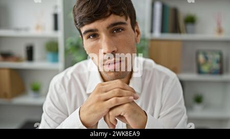 Handsome, young hispanic man sits at office table, embodying confidence. this serious business worker's focused gaze screams success as he takes a bre Stock Photo