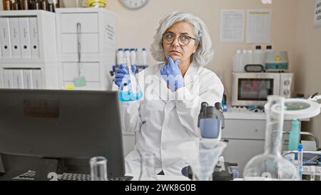 Mature woman scientist contemplating a chemical flask in a laboratory setting. Stock Photo