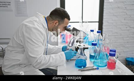 Hispanic man in lab coat analyzing samples using a microscope in a modern laboratory setting. Stock Photo