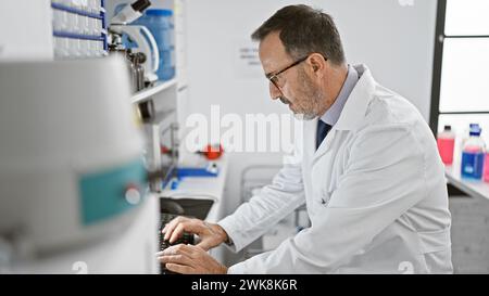 Concentrated middle-aged man with grey hair, immersed in groundbreaking science, harnesses computer power in the buzzing lab environment Stock Photo