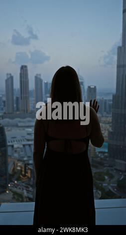 A silhouetted woman gazes at the dubai skyline from an observatory during twilight. Stock Photo