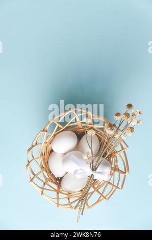 A basket with Easter eggs and dried flowers on blue background, top view. Stock Photo