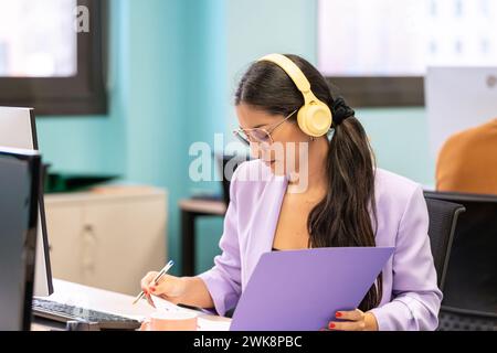Woman working focused with headphones and reviewing papers in a coworking space.  Stock Photo