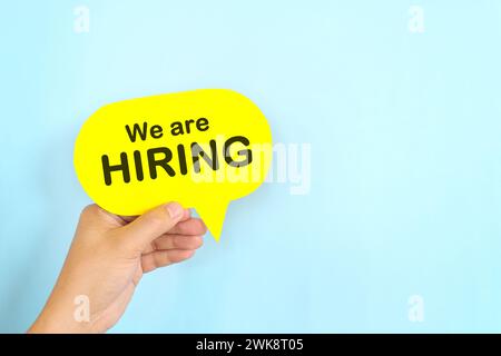 Human hand holding yellow speech bubble with written phrase We are Hiring. Recruitment and job hiring concept. Stock Photo