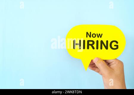 Human hand holding yellow speech bubble with written phrase We are Hiring. Recruitment and job hiring concept. Stock Photo