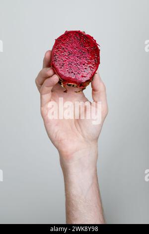 Bright Dragon fruit in male hand on white background. Cut red fleshed pitahaya fruit food closeup Stock Photo