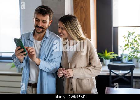 Young happy couple using phone to share social media news at home, doing shopping online. Stock Photo