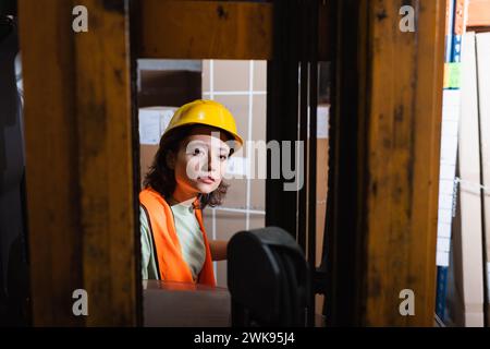 female forklift operator in hard hat and safety vest looking at camera in warehouse, cargo Stock Photo