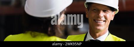 happy middle aged supervisor looking at female colleague in hard hat on blurred foreground, banner Stock Photo