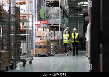 focused supervisor in safety vest and hard hat inspecting warehouse with clipboard, professional Stock Photo