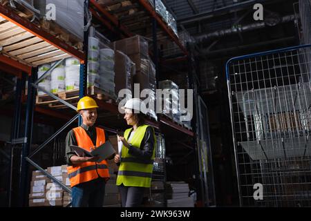 happy professionals in hard hats talking in a warehouse, middle aged boss and subordinate Stock Photo