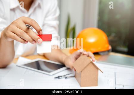 Close up of architect hands holding living house model above blueprint on table. architectural concept. Stock Photo