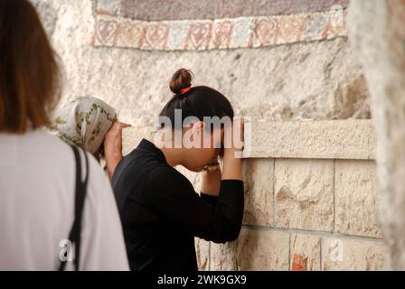 Woman praying to God. Pilgrim in front of an icon. A woman rested her head and hands on the wall during prayer. Stock Photo