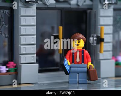 Tambov, Russian Federation - February 18, 2024 A Lego businesswoman minifigure standing in front of a bank while holding a cellphone and a suitcase in Stock Photo