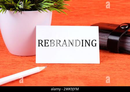 rebranding word written on a business card next to a business card holder, a green flower and a pencil on an orange background Stock Photo