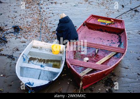 Person sitting on the edge of a rowing boat in Folkestone Harbour at low tide Stock Photo