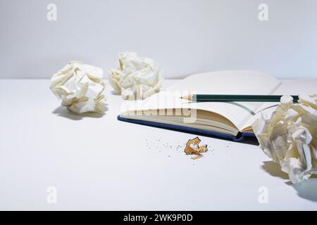 Empty lined notebook with a pencil and crumpled paper balls on a white desk, discarded drafts during the development process in creative writing or bu Stock Photo