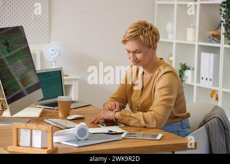 Displeased mature female programmer looking at wristwatch in office Stock Photo