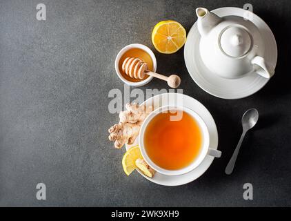 Cup of hot ginger tea with fresh ginger root and lemon on grey background. Stock Photo